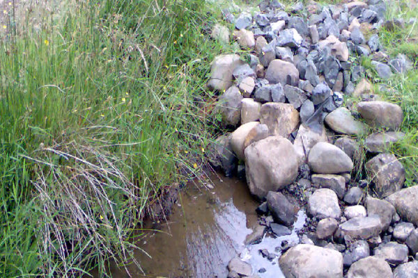 A water extraction point in a watercourse. There are a lot of river stones that can be seen from which the watercourse appears from. The abstraction point is below the river stones.